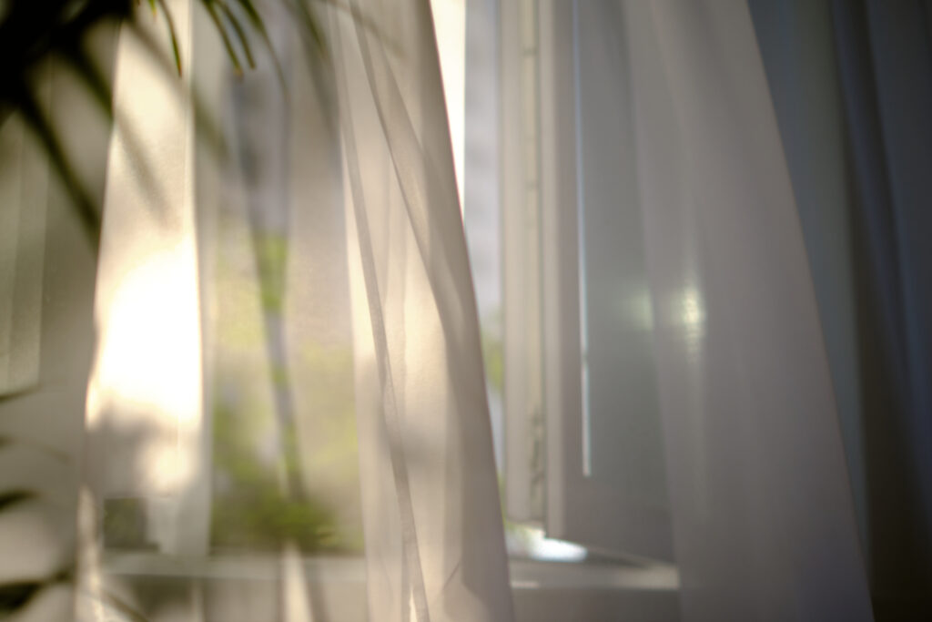 Warm morning sunlight filtering softly through sheer white curtains into a quiet room