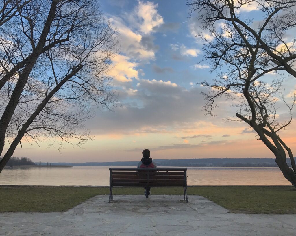 Person sitting quietly on a wooden bench overlooking a serene lake